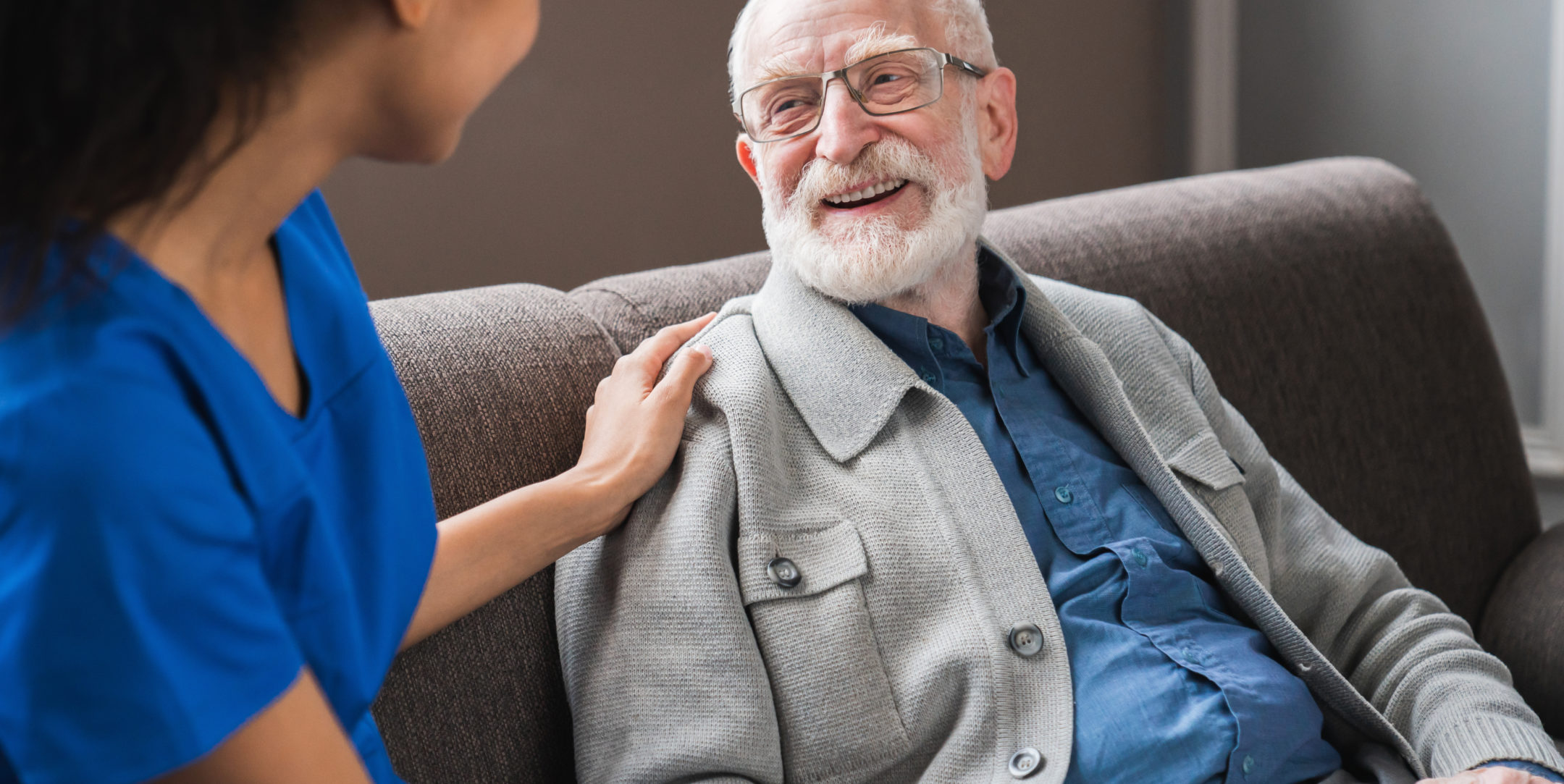 Friendly female caregiver talking chatting to happy senior man in hallway of nursing home.